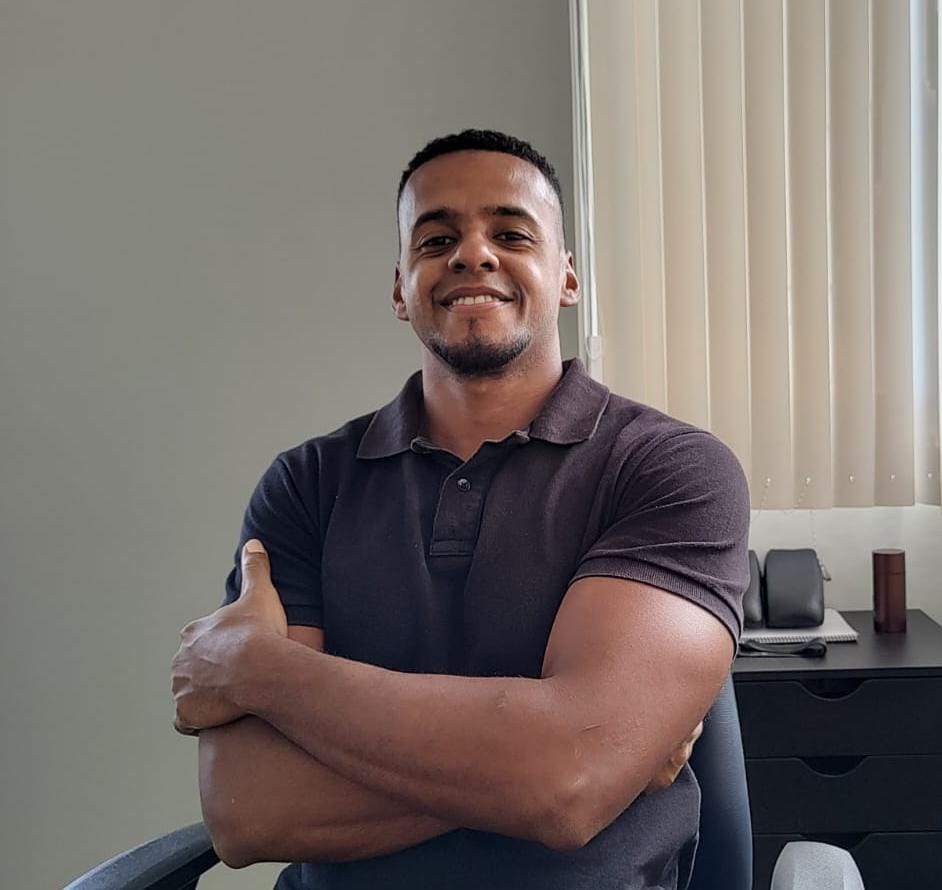 Retrato profissional do Dr. Raphael Nunes, fisioterapeuta da EARFF, camisa polo escura, braços cruzados, sorriso confiante, ambiente de consultório clínico, fotografia corporativa realista