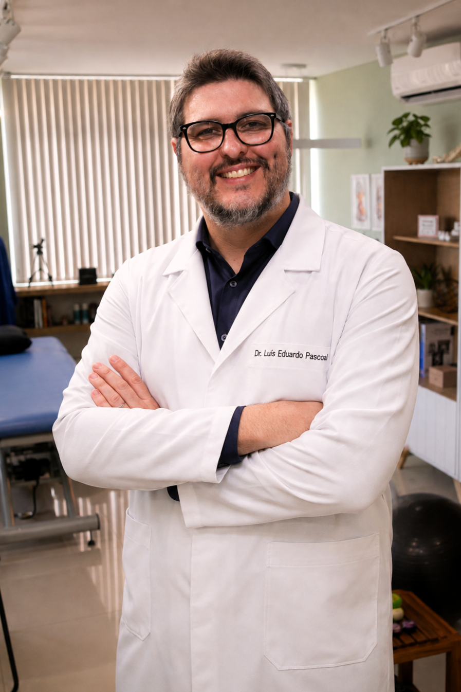 Retrato profissional do Dr. Luís Eduardo Pascoal, fisioterapeuta da EARFF, jaleco branco com crachá de identificação, camisa social escura, óculos de grau, braços cruzados, sorriso confiante, consultório clínico com maca de fisioterapia ao fundo, fotografia corporativa realista